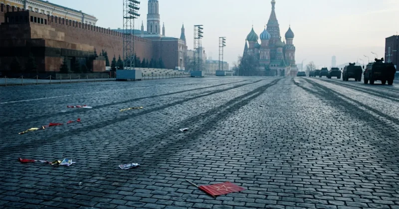 Wide cinematic view of an empty Red Square in Moscow at dawn after a Victory Day parade, with a dropped red flag on the cobblestones and military vehicles withdrawing in the distance