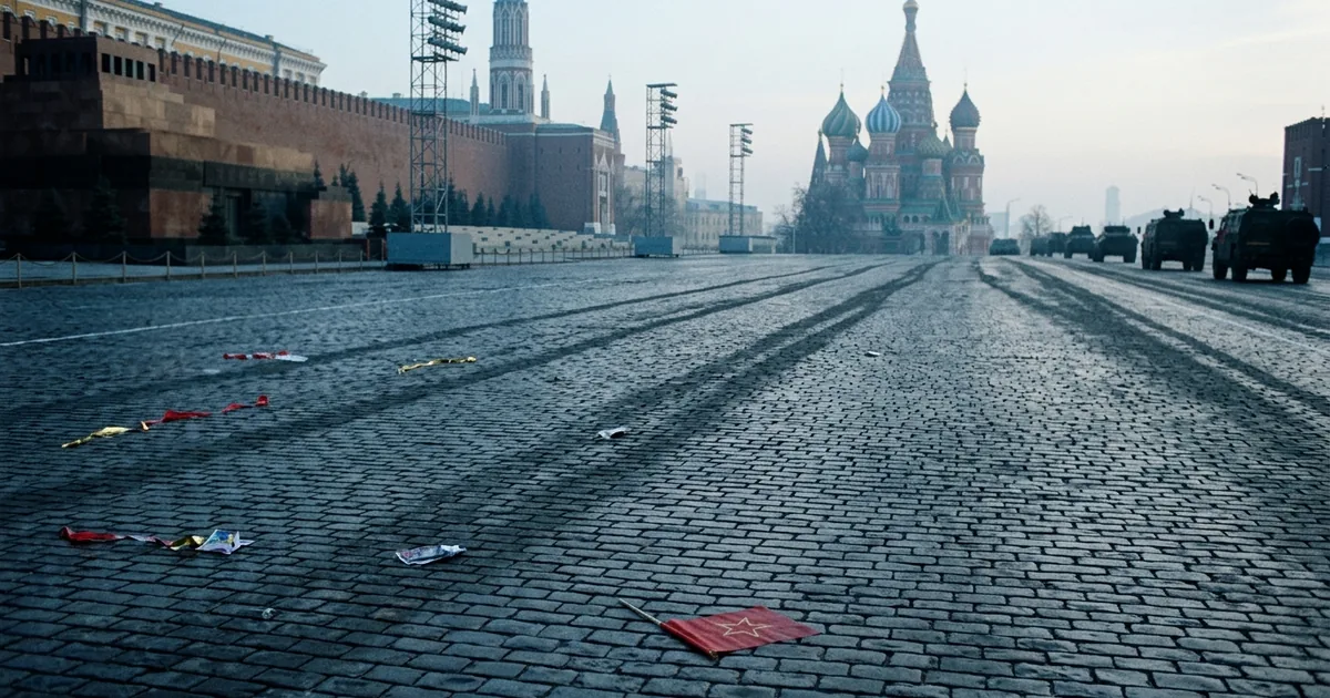 Wide cinematic view of an empty Red Square in Moscow at dawn after a Victory Day parade, with a dropped red flag on the cobblestones and military vehicles withdrawing in the distance