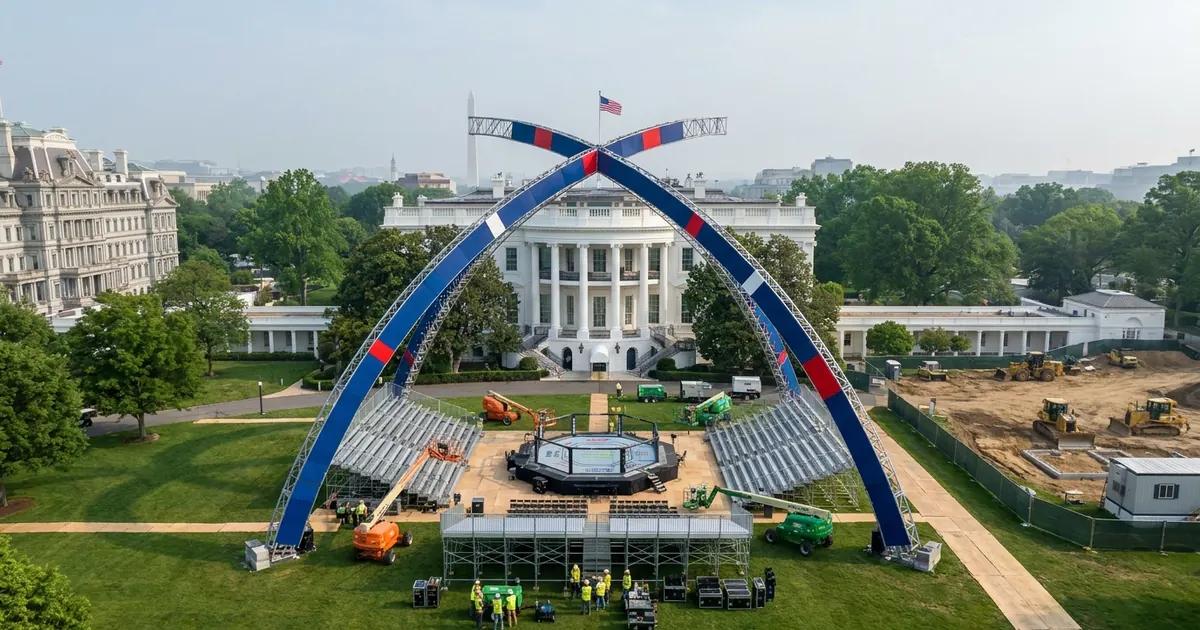 Aerial UPI-style press photograph of the White House South Lawn: two intersecting parabolic steel arches clad in deep blue with red and white accents form a gateway portal framing the South Facade of the White House, with the UFC Freedom 250 octagon cage and bleacher seating built beneath, construction workers in high-visibility vests gathered around the stage, the Eisenhower Executive Office Building visible on the left, the demolished East Wing site cleared to bare dirt with yellow Caterpillar bulldozers and chain-link fencing on the right, and the Washington Monument hazy in the deep background