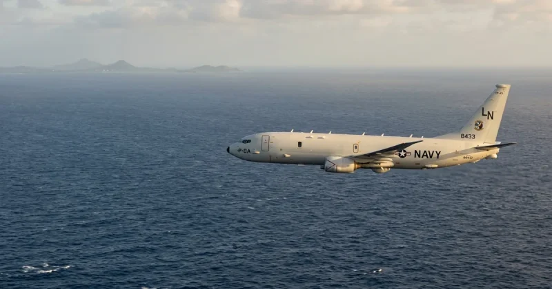 A US Navy P-8A Poseidon maritime patrol aircraft in level flight over the Caribbean Sea at golden hour, with a distant tropical coastline visible on the horizon