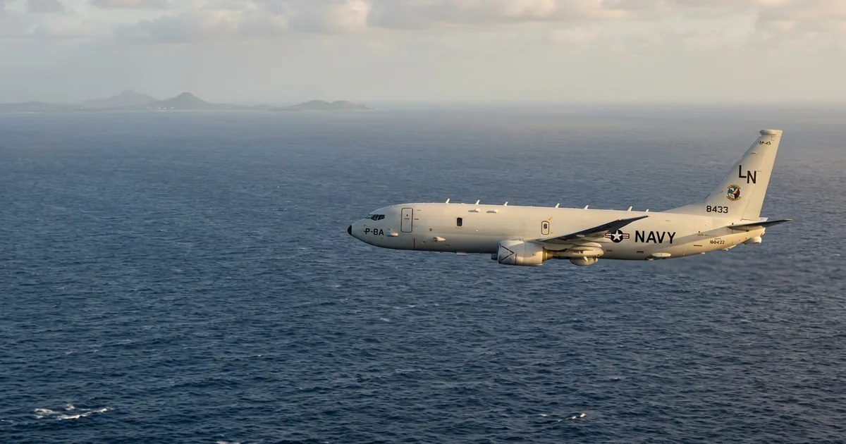 A US Navy P-8A Poseidon maritime patrol aircraft in level flight over the Caribbean Sea at golden hour, with a distant tropical coastline visible on the horizon