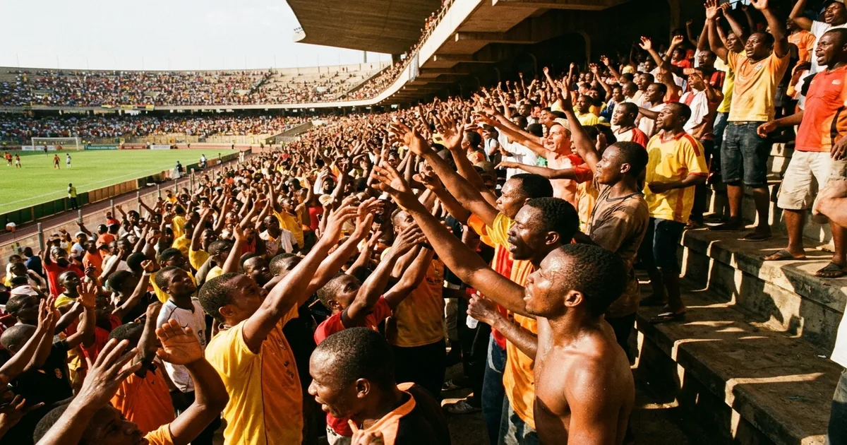 Soccer fans in a sun-drenched stadium raising their hands in the heat with no water bottles visible