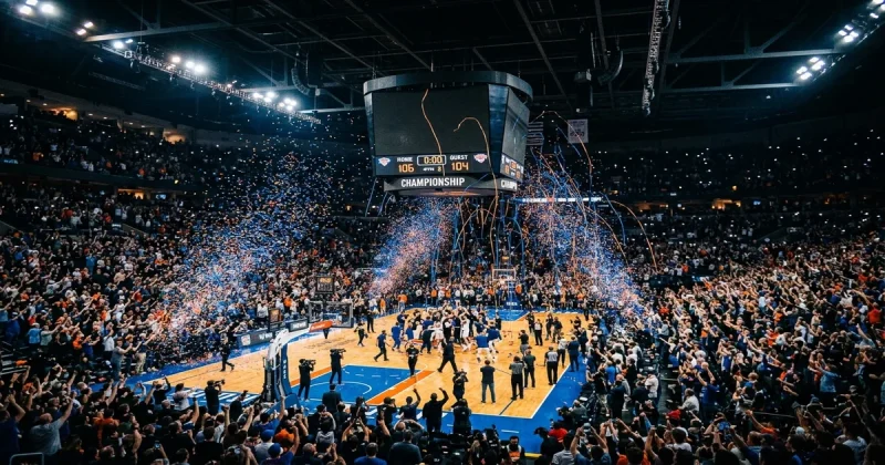 Packed basketball arena with blue and orange confetti falling after a championship-clinching moment