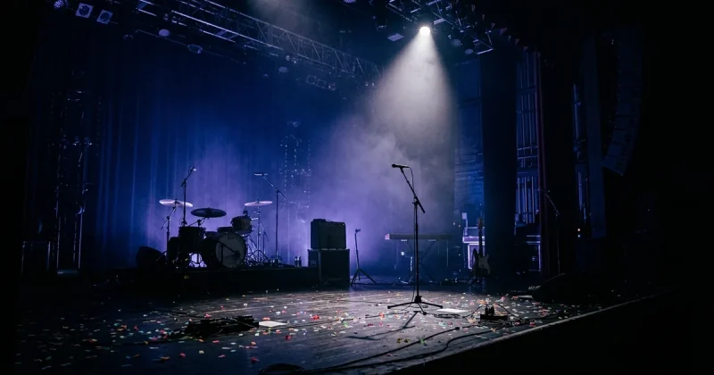 Empty concert stage illuminated by a single spotlight with instruments silhouetted and confetti on the floor