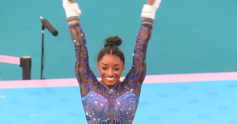 Simone Biles smiling with her arms raised in celebration at the 2024 Paris Olympics
