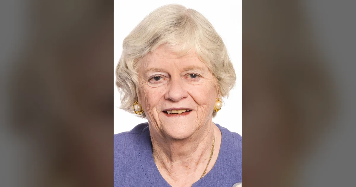 Official portrait of Ann Widdecombe smiling in a lavender jacket with pearl earrings against a blurred backdrop