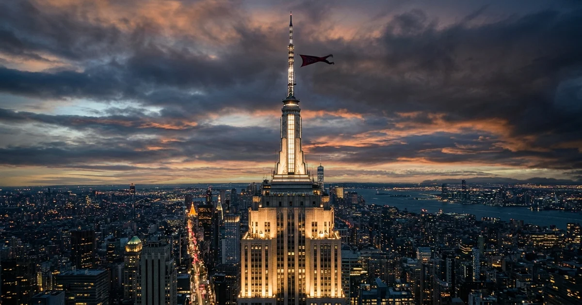 Empire State Building spire against dramatic twilight sky with small banner fluttering near the top, city lights below