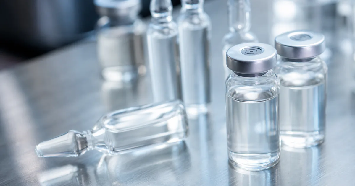 Clear glass laboratory vials containing translucent liquid on a stainless steel surface under clinical lighting