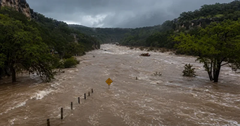 Aerial view of flooded Guadalupe River valley in Texas Hill Country with muddy brown floodwaters and emergency rescue boat