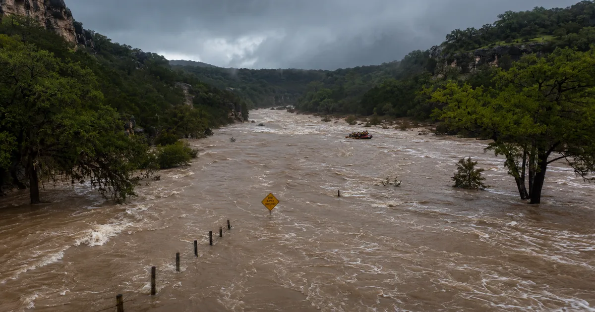 Aerial view of flooded Guadalupe River valley in Texas Hill Country with muddy brown floodwaters and emergency rescue boat