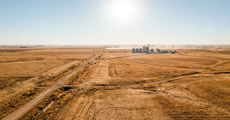Aerial view of dry cracked farmland and grain silos shimmering under a blazing sun in the American heartland