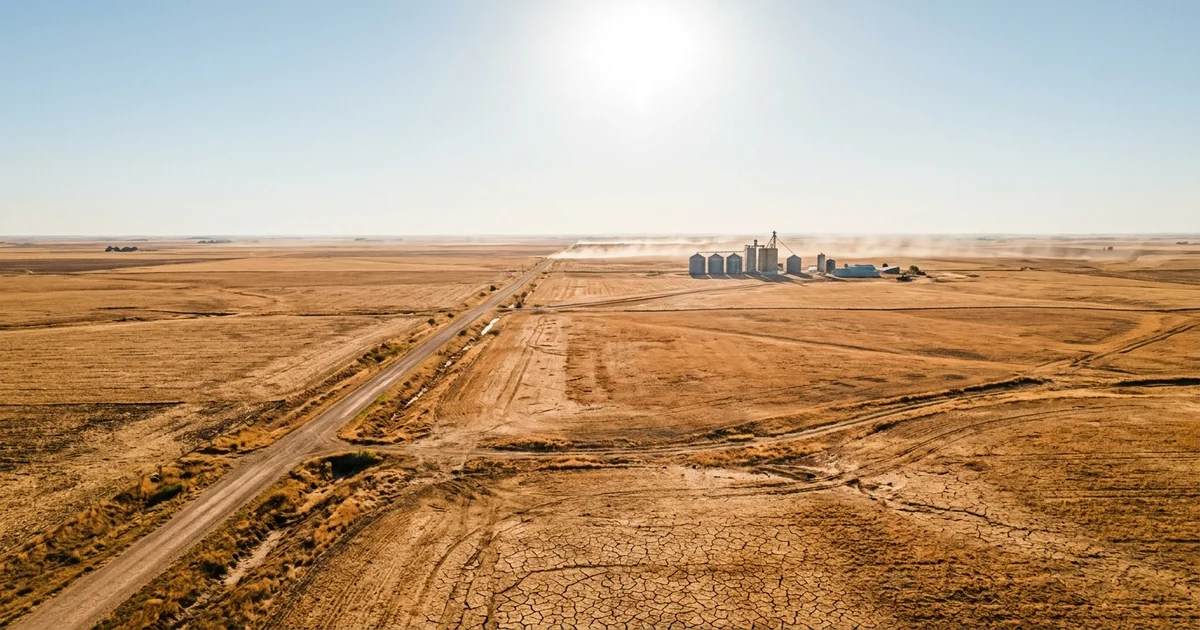 Aerial view of dry cracked farmland and grain silos shimmering under a blazing sun in the American heartland