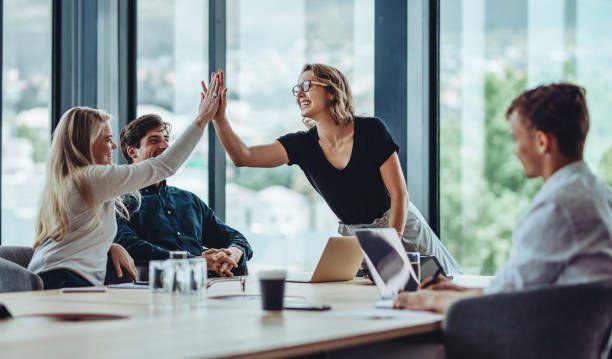 Two coworkers high-five across a meeting table while teammates look on