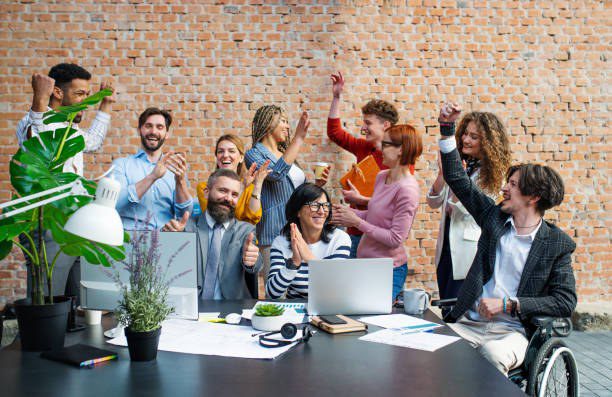 A diverse office team cheering and applauding around a desk in a brick-walled workspace