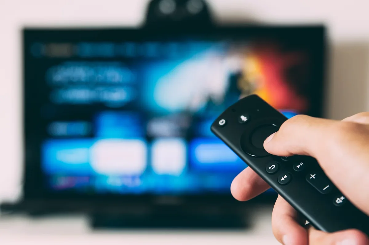 A hand holding a remote in front of a television showing a streaming platform interface