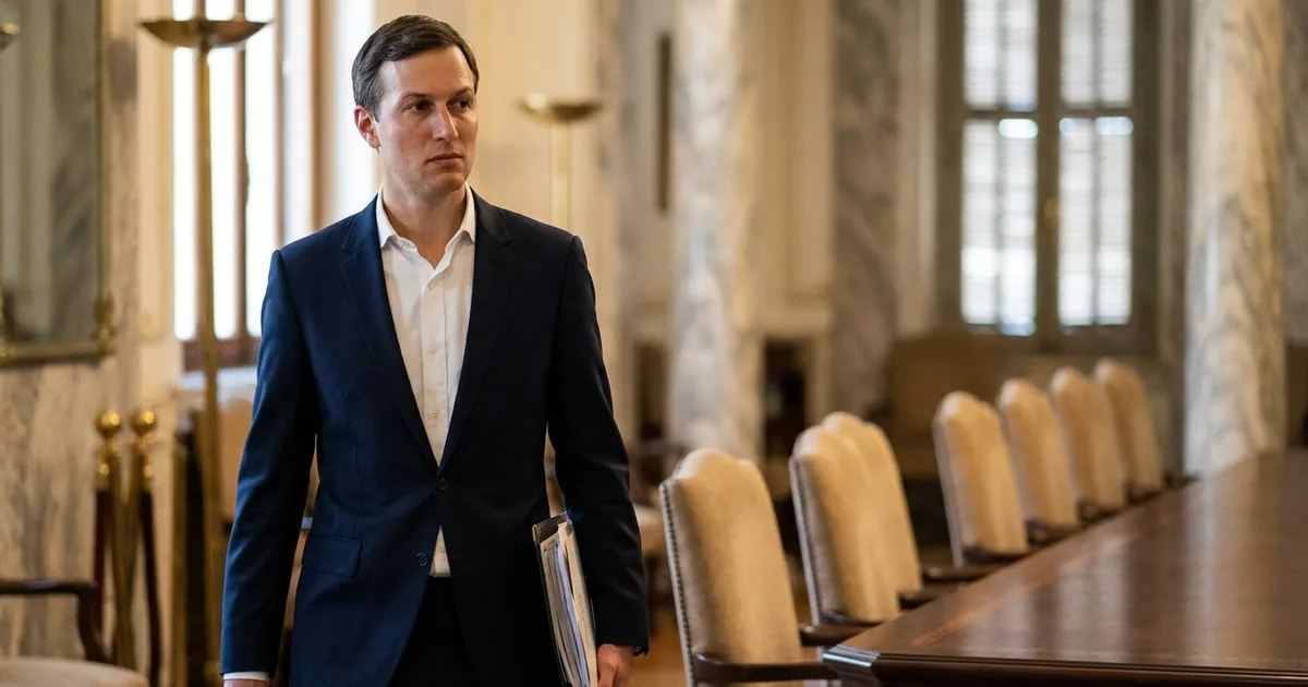 A dark-suited American envoy walks past an empty negotiating table in a marble government reception room