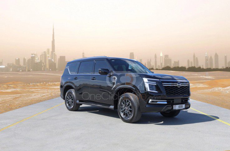 Black full-size Nissan Patrol SUV parked on a desert road with the Dubai skyline behind it