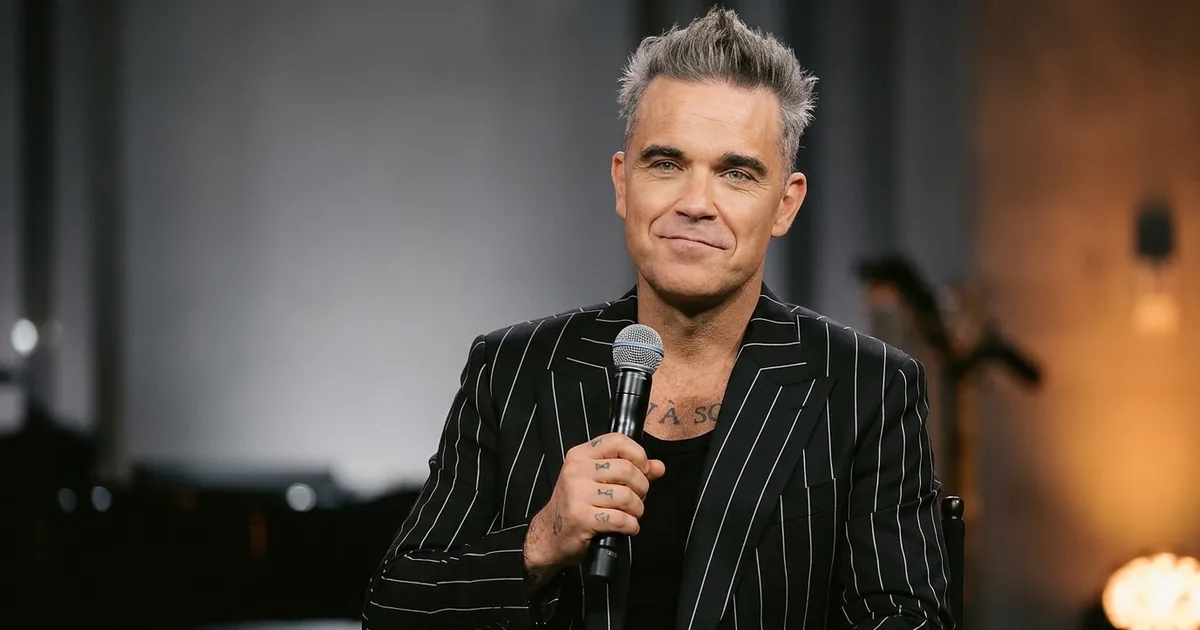 A greying pop singer in a dark pinstriped jacket holds a microphone mid-sentence with a wry half-smile