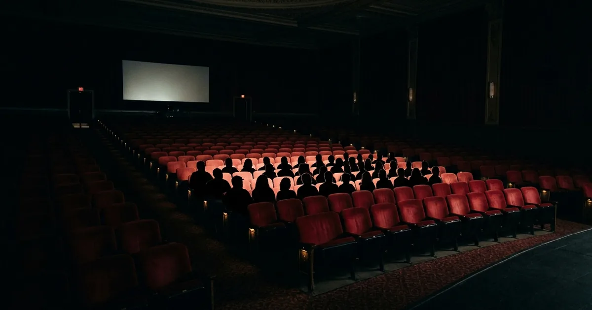 A darkened cinema auditorium where a small cluster of center rows is filled with silhouetted moviegoers while hundreds of red seats around them sit empty