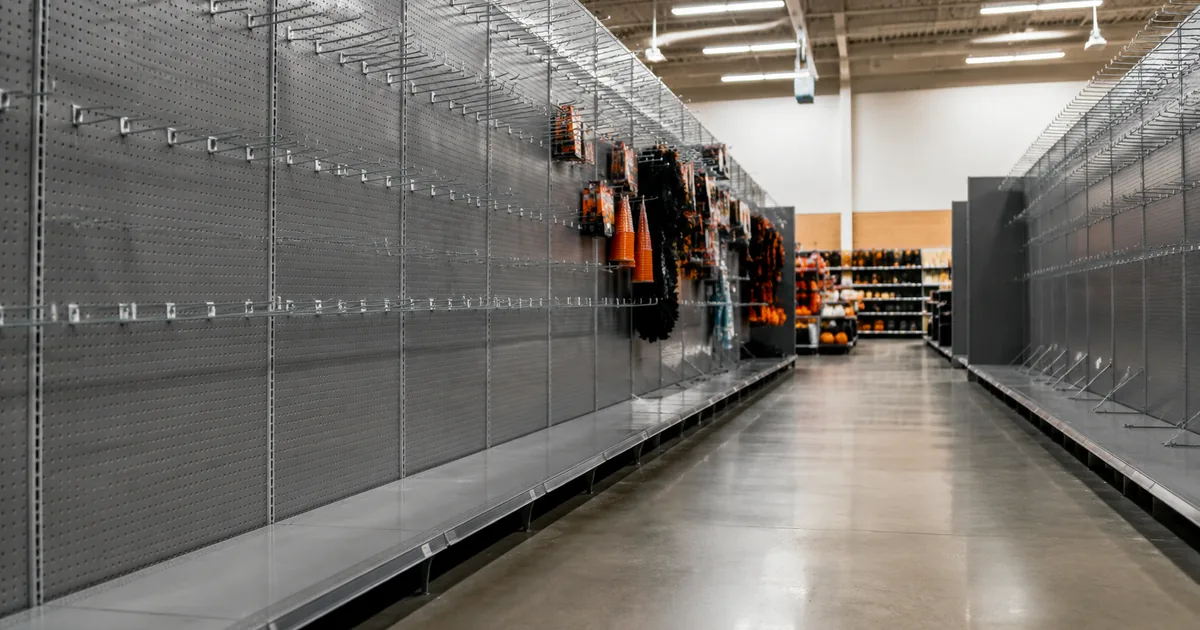 Rows of bare metal display pegs in a retail store seasonal aisle with a few orange and black packages remaining at the far end