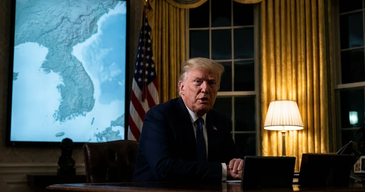 President Donald Trump seated at the Resolute Desk in a darkened Oval Office, speaking, with a blue-lit map of the Korean peninsula displayed on a screen behind him