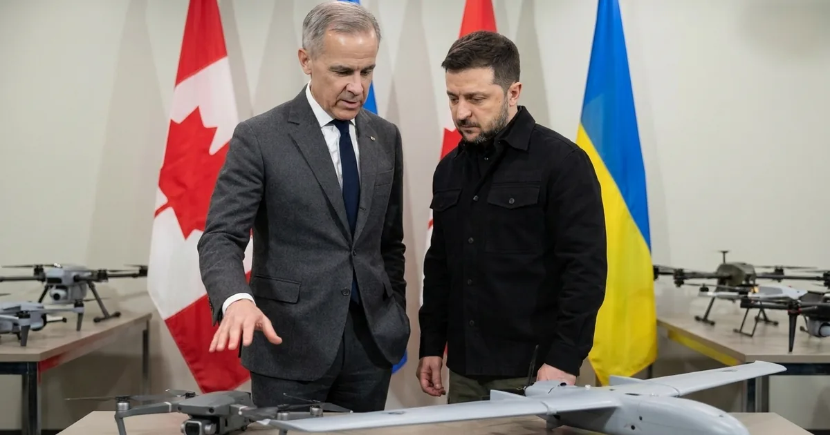 Mark Carney gestures toward a quadcopter and a fixed-wing drone on a display table as Volodymyr Zelenskyy looks on, with Canadian and Ukrainian flags behind them