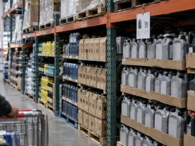 Stacked cases of motor oil on steel warehouse shelving with a small purchase-limit sign clipped to the shelf edge