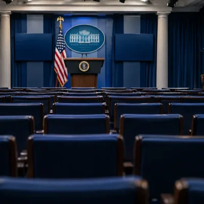 The White House press briefing room with rows of empty blue seats, a lectern at the front and camera tripods standing empty along the side wall