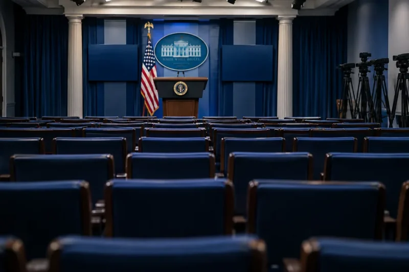 The White House press briefing room with rows of empty blue seats, a lectern at the front and camera tripods standing empty along the side wall