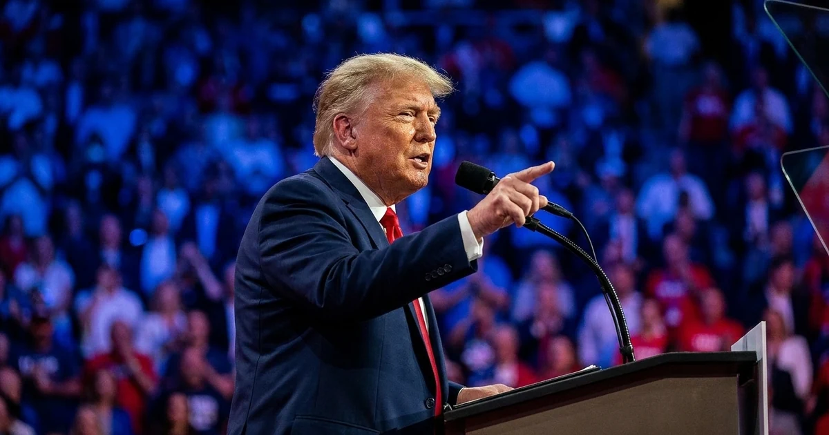 Donald Trump pointing while speaking at a lectern in front of a packed arena crowd lit in blue and red stage light