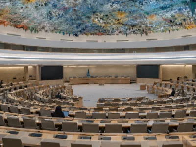 Rows of empty curved delegate desks beneath the colorful stalactite ceiling of the UN Human Rights Council chamber in Geneva
