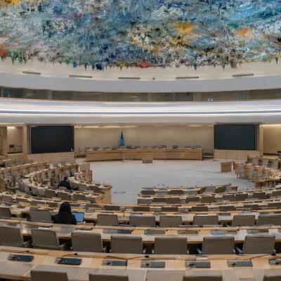 Rows of empty curved delegate desks beneath the colorful stalactite ceiling of the UN Human Rights Council chamber in Geneva