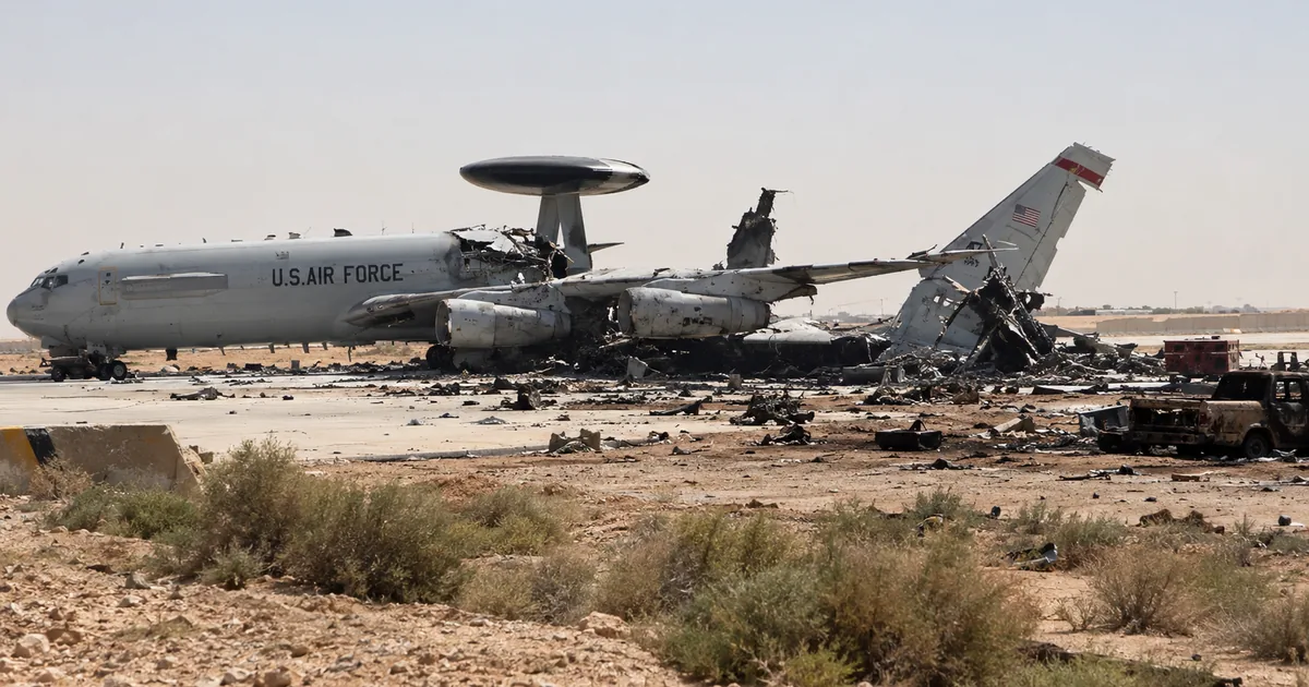 Illustration of a gray U.S. Air Force E-3 Sentry radar plane on a desert air base apron with its rear fuselage and tail torn apart, debris and a burned truck nearby
