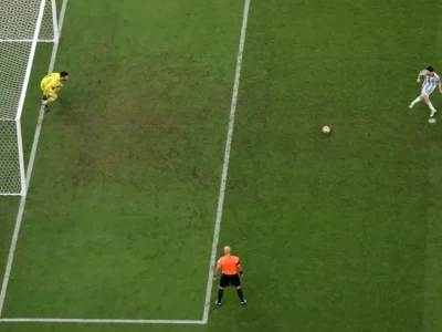 Aerial view of a penalty kick with the goalkeeper diving early and the referee watching from the edge of the box