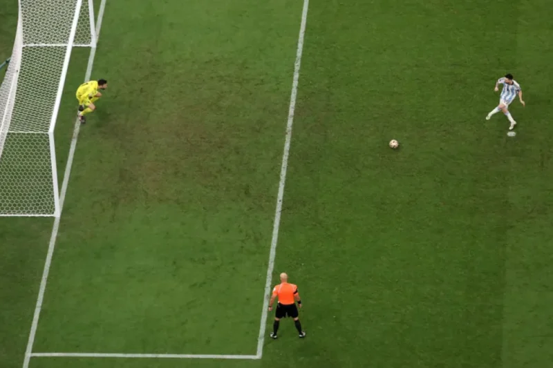 Aerial view of a penalty kick with the goalkeeper diving early and the referee watching from the edge of the box