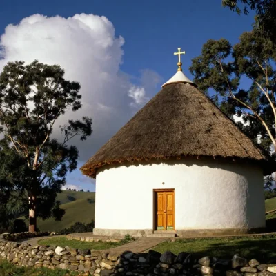 Illustrative image of a round whitewashed Ethiopian Orthodox church with a thatched roof and a gold cross on a green highland hillside under a deep blue sky