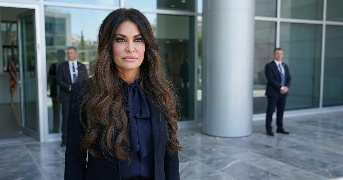 Kimberly Guilfoyle in a navy blazer and bow blouse stands outside the glass entrance of the U.S. Embassy in Athens with two men in dark suits behind her