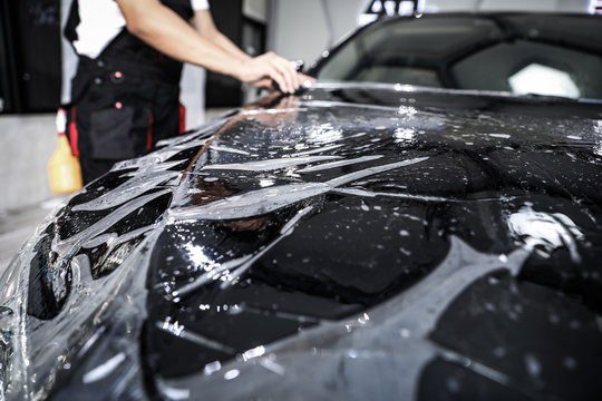 Clear paint protection film being applied over the hood and fender of a dark car
