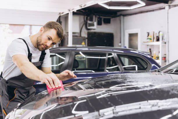 Technician polishing the glossy dark paint of a car in a detailing bay