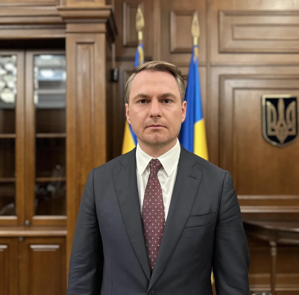 Ruslan Kravchenko, former Prosecutor General of Ukraine, in a wood-panelled office with the Ukrainian flag and coat of arms