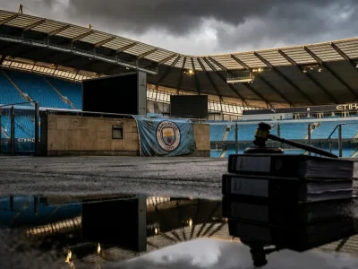 Empty Etihad Stadium stands under storm clouds, a Manchester City banner on the wall, with a stack of legal files and a gavel in the foreground