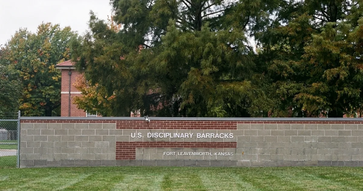 The U.S. Disciplinary Barracks entrance sign on a block-and-brick wall at Fort Leavenworth, Kansas, with trees and a brick building behind it