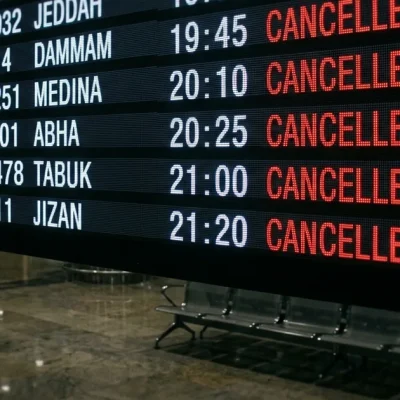 Illustration of an airport departures board in a darkened terminal with flights to Jeddah, Dammam, Medina, Abha, Tabuk and Jizan all marked cancelled in red