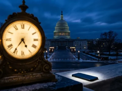 An antique clock and a smartphone on a marble ledge with the US Capitol dome in pre-dawn darkness