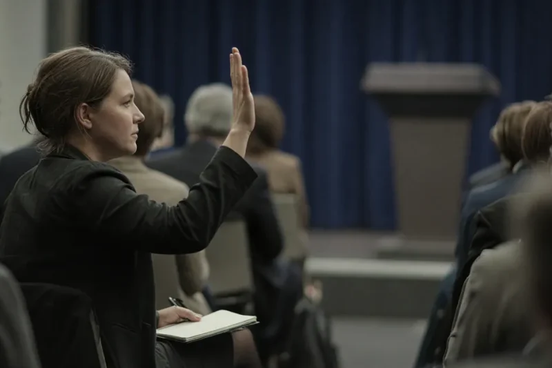 A reporter raises a hand in the White House briefing room as the lectern stands empty in the background
